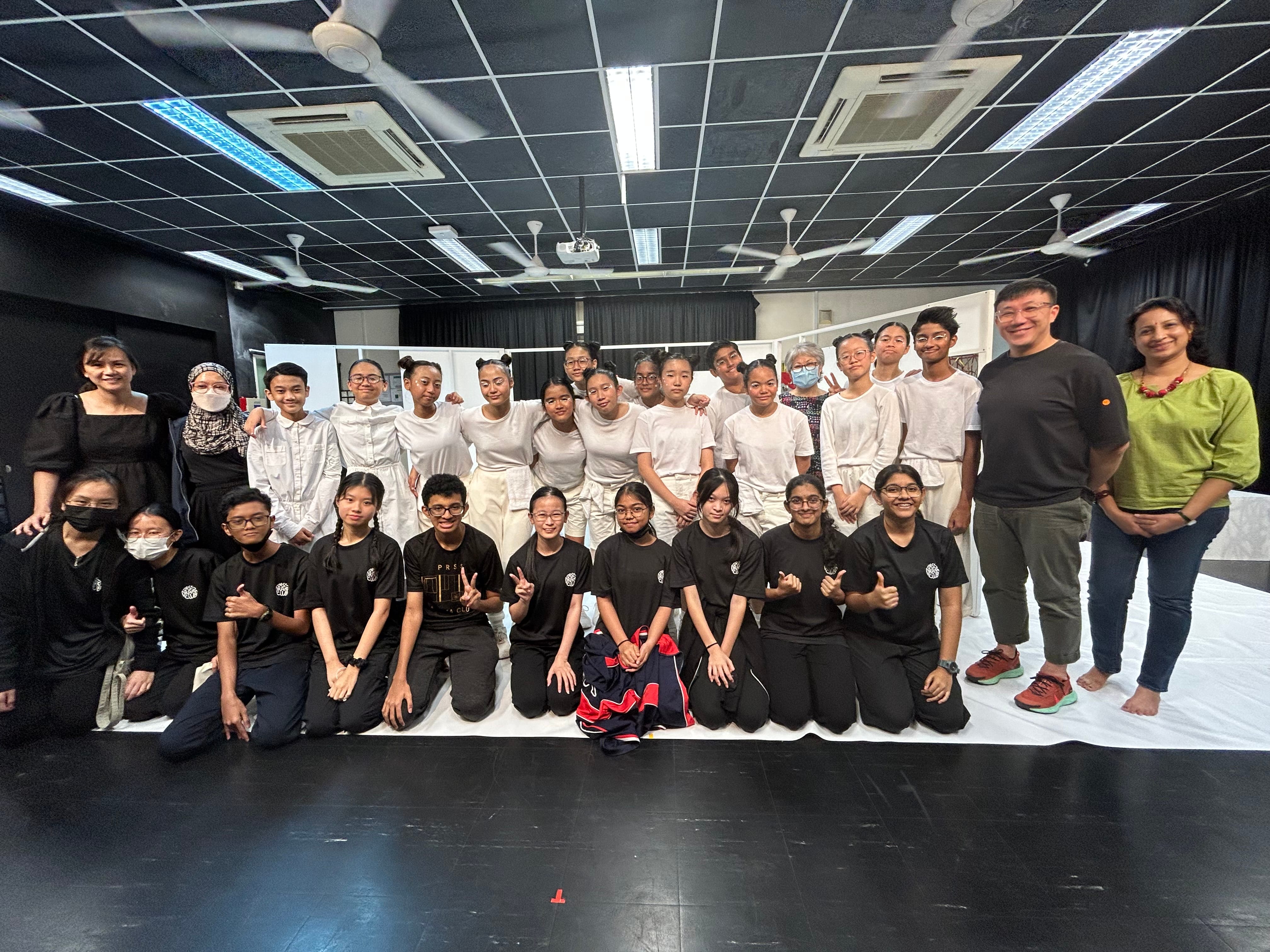 Group photo of students in black and white outfits posing in a studio, with two adults at right.
